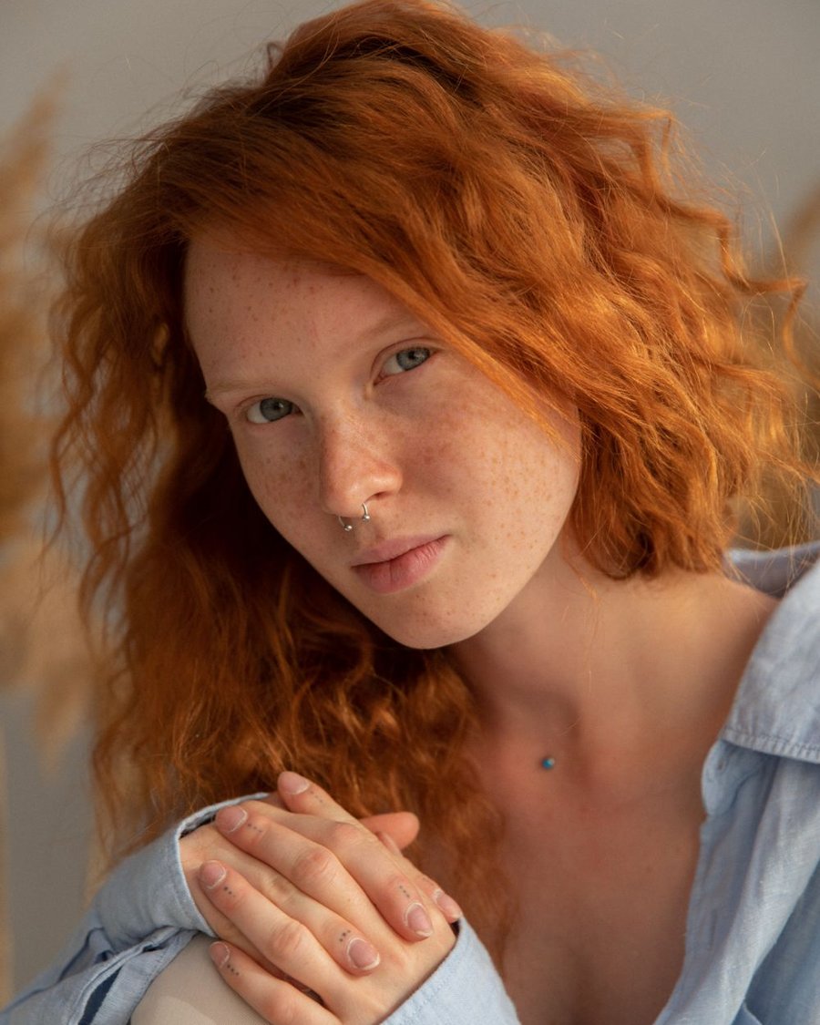 Mujer pelirroja con pecas y camisa celeste, con luz cálida
