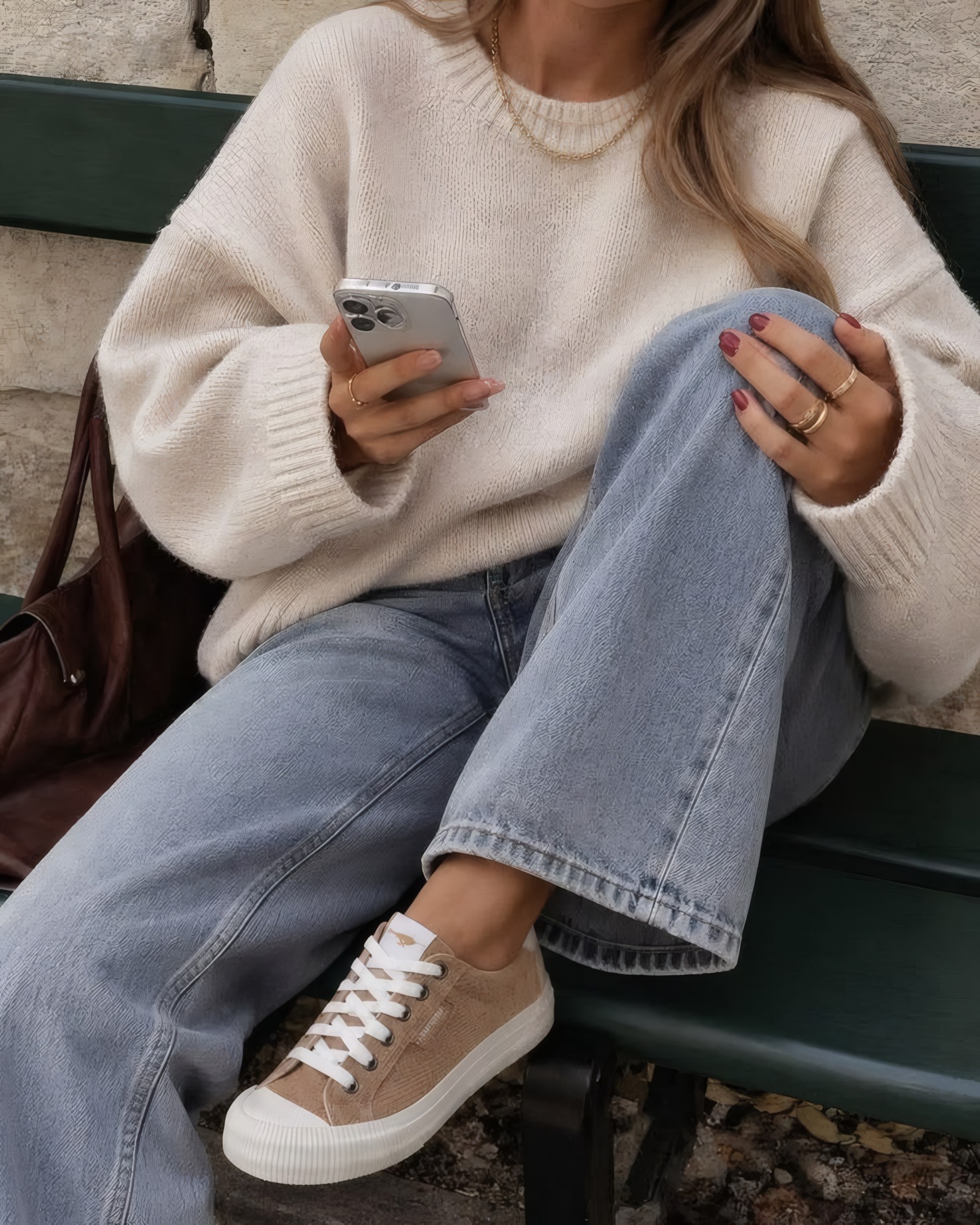 Mujer con sweater amplio de punto, jean ancho y zapatillas, sentada en un banco