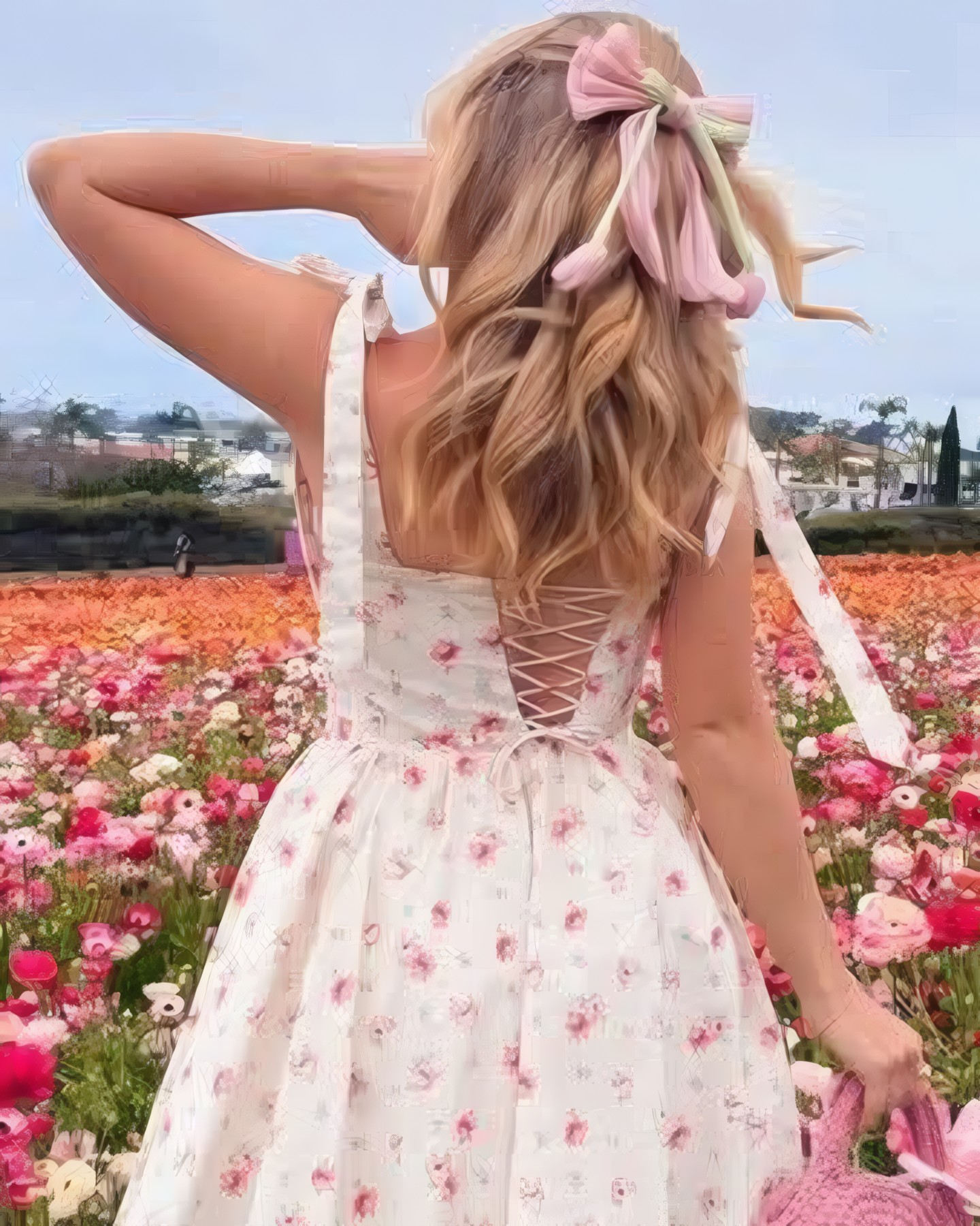Mujer de espaldas con vestido floral corto, moño rosa en el pelo y cartera tejida, en un campo de flores